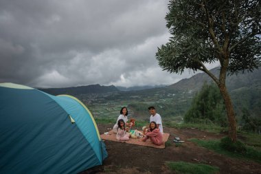 Bir aile, doğa harikalarıyla çevrili güzel bir doğa ortamında çadırlarının önünde güzel bir pikniğin tadını çıkarıyor.