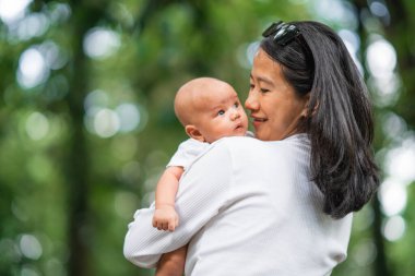 Bir annenin sevgi dolu bir şekilde tapılası bebeğini canlı, yeşil bir ortamda tutması.