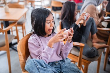 Parlak bir kafede akıllı telefonuyla etkileşime giren genç bir kız.