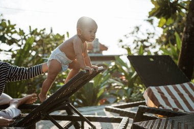 Neşeli ve şakacı bir bebek açık hava mobilyalarına tırmanıyor, neşeyle doğayı kucaklıyor.