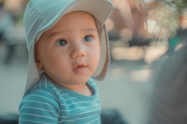 Neşeli bir bebek, parlak mavi gözleri ve sevimli bir güneş şapkası ile güneşli bir günün tadını çıkarıyor.