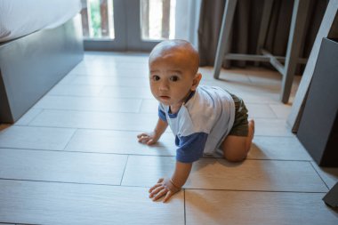 Mutlu bir bebek fayanslarla döşenmiş bir zeminde geziniyor, neşe dolu bir kapalı mekanı keşfediyor.