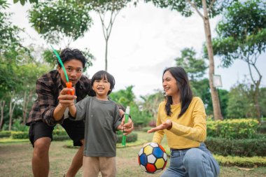 Bir baba, anne ve oğul parkta baloncuk ve top oynuyorlar.
