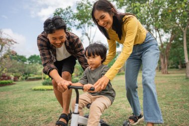 Küçük çocuk dışarıda anne ve babasıyla bisiklet sürmeyi öğreniyor.