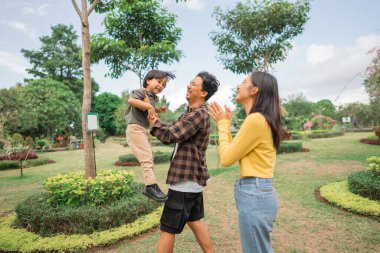 Küçük çocuk parkta oynarken babasının elleriyle kaldırdı.