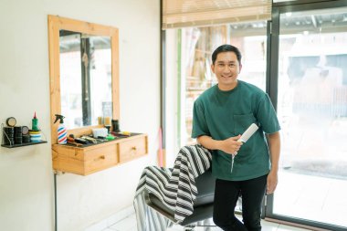 Bir adam berber dükkanında elinde saç kurutma makinesiyle duruyor. Saç şekillendirmek için kullanmaya hazır.