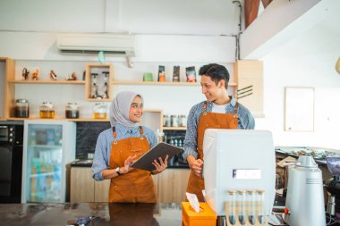 Peçeli bayan garson, kahve dükkanında kahve yapan bir erkek garsonla tablet kullanıyor.