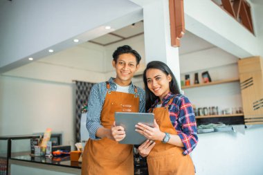 Önlük takan kadın ve erkek esnaf kahve dükkanında birlikte tablet kullanıyorlardı.