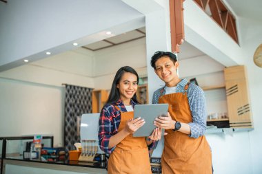 Endonezyalı kadın ve erkek bir kafede tablet kullanarak gülümsüyorlar.