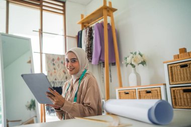 Güzel peçeli Asyalı moda tasarımcısı atölyede bir tablet bilgisayar kullanıyor.