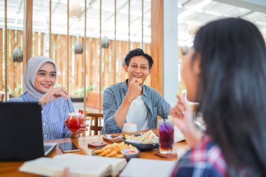 Erkek ve kadın üniversite öğrencileri bir kahve dükkanında birlikte kahvaltı ediyorlar.