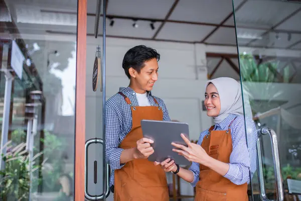 Peçeli kadın ve erkek garson birlikte tablet kullanıyorlar. Bir kahve dükkanının önünde duruyorlar.