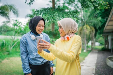 İki neşeli arkadaş, yeşil bir parkta güneşli bir günün tadını çıkarırken akıllı telefondan birbirlerine bağlanıyorlar.