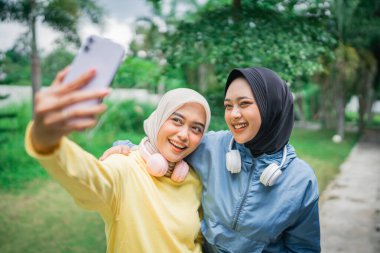 İki yakın arkadaş, güzel yeşil bir açık hava parkında selfie çekmekten mutluluk duyuyorlar.
