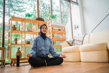 Bir kadın, aydınlık ve davetkar bir oturma odasında huzur içinde meditasyon yapıyor.