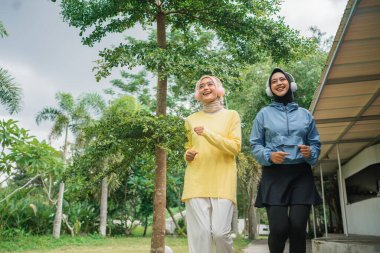 İki arkadaş, güzel yeşillikler ve ağaçlar arasında birlikte yürümekten mutluluk duyuyorlar.