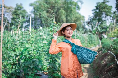 Neşeli bir kadın, elinde bir sepet tutarak verimli, canlı bir bahçede eğleniyor.
