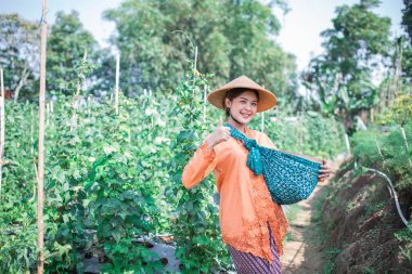 Neşeli bir çiftçi güzel, yemyeşil bir bahçede renkli bir sepetle poz verir.