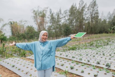 Neşeli bir kadın, yemyeşil, canlı bir çevrede gelişen sebze çiftliğini gururla sergiliyor