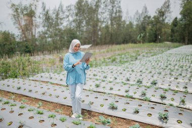 Parlak mavi elbiseli bir kadın seradaki bitkileri dikkatle inceliyor.