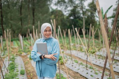 Kendine güvenen bir kadın, verimli ve canlı bir ortamda modern aletlerle gelişen çiftliğini yönetiyor.