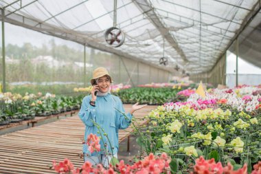Neşeli bir bahçıvan, canlı bir serada çiçek açan orkidelerle çevrilidir ve dinginlik yaratır.