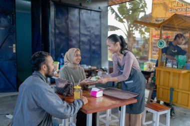 Müşteriler ve çalışanlar arasında dostça etkileşim olan rahat bir kafe atmosferi.