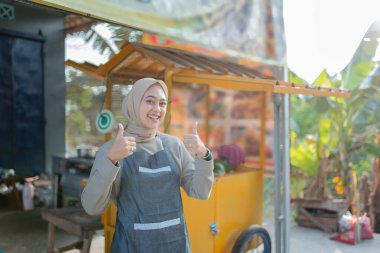 Neşeli bir barista, parlak bir gülümseme ile renkli kahve sepetine başparmak sallar.