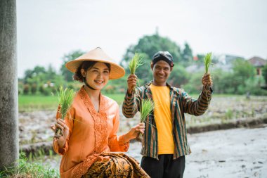 İki neşeli çiftçi, çarpıcı bir manzaranın ortasında canlı ve sağlıklı pirinç fidelerini gururla sergiliyor.