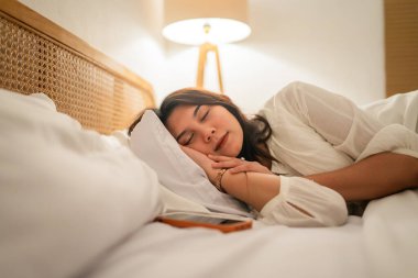 Bir kadın rahat bir yatak odasında huzur içinde uyur. Huzur ve sükunet saçar.