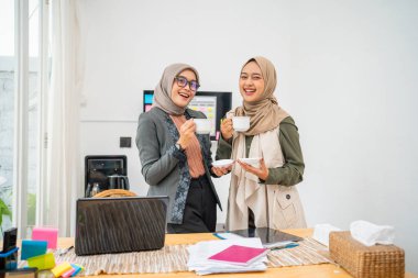 İki kadın kahve eşliğinde kaynaşıyor. Parlak, şık bir çalışma alanında, birlikte vakit geçiriyorlar.