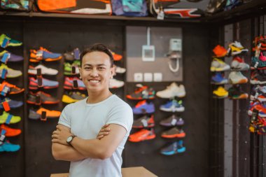 Asyalı spor mağazası çalışanı gülümseyen yüzüyle ve çapraz koluyla