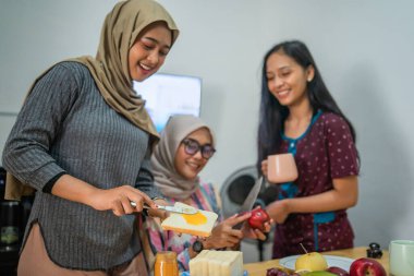 Üç yakın arkadaş, modern bir mutfakta keyifli bir yemek pişirme deneyimi paylaşıyor.