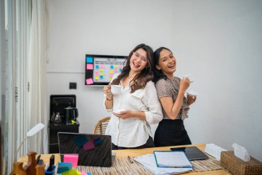 Işıl ışıl bir ofiste, iki neşeli kadın kahve içerken, birbirleriyle vakit geçirirler.