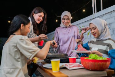 Arkadaşlar mutlu bir şekilde yemek pişirir ve açık havada neşeli anlar paylaşırlar.