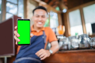 El kafesi garsonu arka planı bulanık, boş ekranlı bir telefon tutuyor.