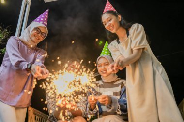 Dostlar neşeli bir şekilde havai fişekler ve parti şapkalarıyla şenlikli bir atmosfer altında toplanır.