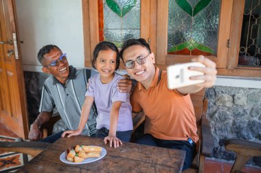 Mutlu Asyalı adam telefonu kullanarak babası ve kızıyla fotoğraf çekiyor.