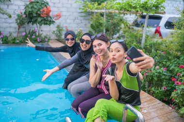 Keyifli ve enerjik bir arkadaş grubu havuz kenarında neşeyle selfie çekiyor.