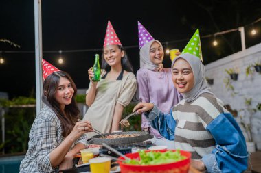 Canlı bir grup arkadaş, güzel sicim ışıkları altında canlı bir barbekü partisinin keyfini çıkarıyorlar.