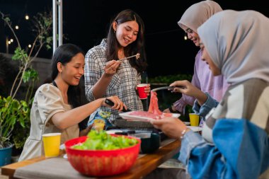 Canlı bir arkadaş toplantısı, hepsi lezzetli yemeklerin tadını çıkarıyor güzel gökyüzünün altında.