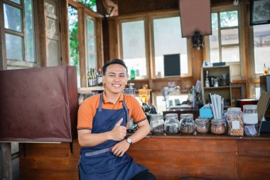 Bir kafede çalışan Asyalı erkek barista, el hareketi yapıyor.