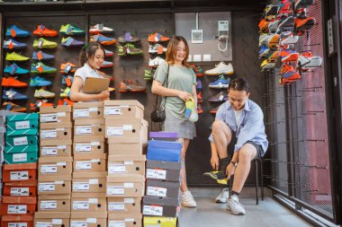 Erkek müşteri spor ayakkabılarını dener. Eşi ve satış elemanı eşliğinde.