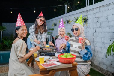 Friends celebrating together with food, colorful hats, and laughter in the beautiful outdoors clipart