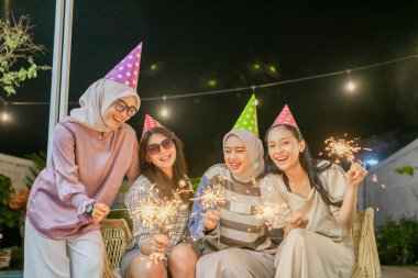 Dört arkadaş neşeli bir geceyi havai fişekler ve renkli parti şapkalarıyla kutluyor.