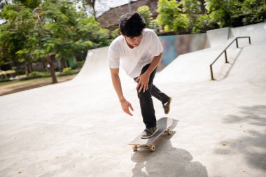 Yetenekli bir patenci açık mavi gökyüzünün altındaki canlı bir kaykay parkında etkileyici numaralar yapıyor.