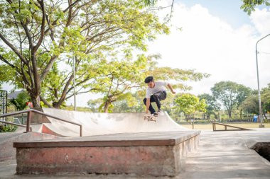 Bir kaykaycı, güneşli bir parkın kaykay yerinde havada süzülüyor.