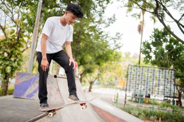 Genç bir kaykaycı çevrenin yeşilliklerle çevrili olduğu canlı bir kaykay parkında numaralar yapıyor.