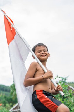 Endonezya 'nın bağımsızlık kutlamalarında beyaz arka planda kırmızı ve beyaz bayrak taşıyan yakışıklı çocuk.