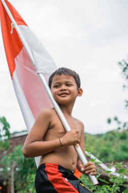 Özgürlük kutlamaları sırasında Endonezya bayrağı taşıyan üstsüz gülümseyen çocuğun yakın plan fotoğrafı.